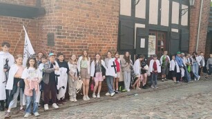 Grupa dwudziestu pięciu uczniów klasy piątej stoi wzdłuż ściany Krzywej Wieży w Toruniu.