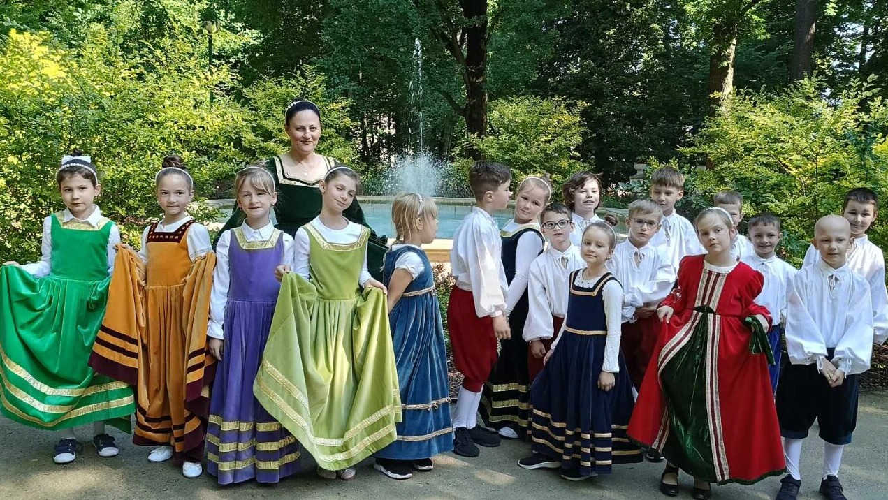 Grupa 17 uczniów w kostiumach typu renesansowego stoi w Parku Saskim
