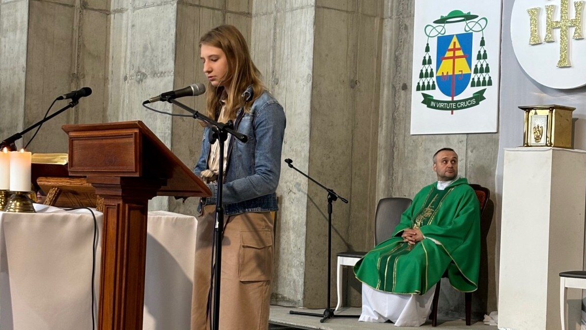 Msza- zakończenie roku, kościół, uczennica stoi przy ambonce i czyta tekst, ksiądz siedzi z tyłu w zielonym ornacie